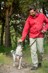 A guy in a red jacket walks his dog in the woods