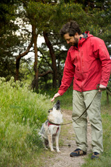 A guy in a red jacket walks his dog in the woods