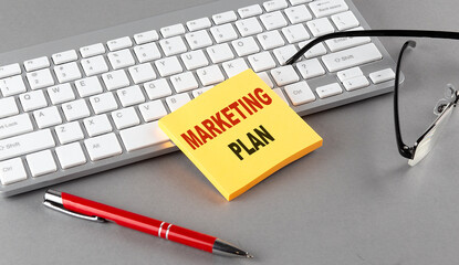 MARKETING PLAN text on a sticky with keyboard, pen glasses on grey background
