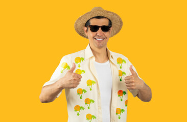 Latin man on vacation wearing floral shirt hat sunglasses over isolated yellow background doing happy thumbs up gesture with hands. Approving expression looking at the camera with showing success.