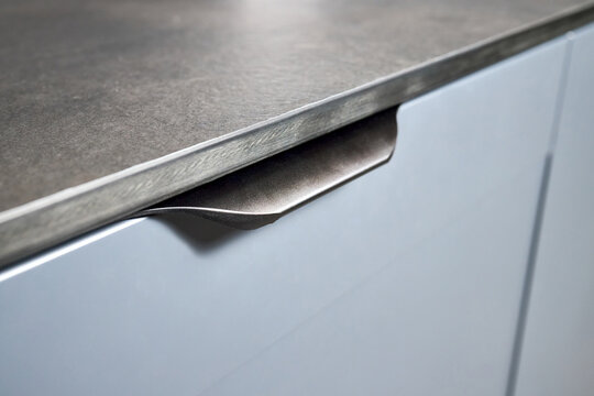 Pull out rack cabinet drawer handle closeup. Flush up slip handle finger pull profile handle of contemporary kitchen drawer with grey blue facade and compact high pressure laminate HPL countertop.