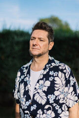 Portrait of a mature man with sideburns dressed in Hawaiian shirt outdoors in a garden. Men's fashion and beauty in travel and vacation.