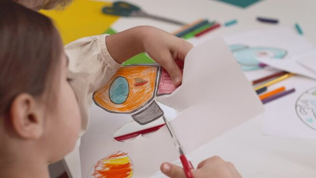 Preschool girl cutting out picture of space rocket while crafting in classroom