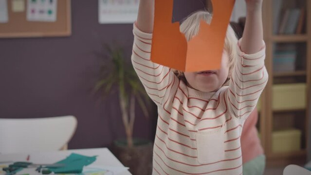 Medium portrait of happy Caucasian little boy posing for camera with his head in space rocket shaped colored paper at classroom