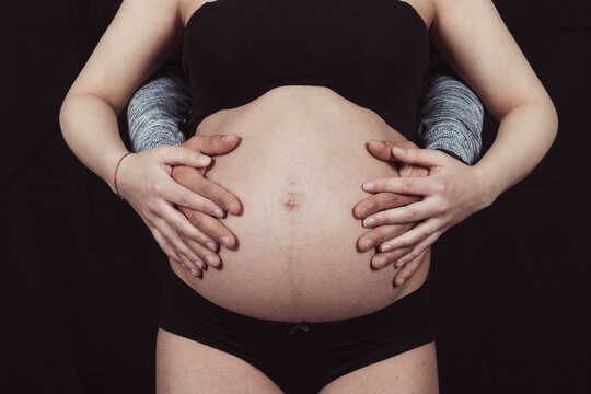 Studio image of pregnant couple. Husband touching his wife's belly with his hands. Half-pregnant hands of mother and father.