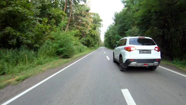 Follow to white car riding through forest road. SUV driving at beautiful countryside wood route on summer. Holidays journey to nature. Scenic landscape way. Concept of family travel at auto. Aerial