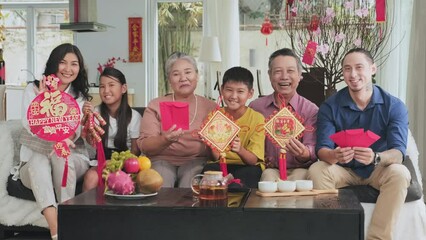 Group portrait of joyous multigenerational family sitting on couch in living room, holding traditional Tet decorations and happily smiling on camera while celebrating holiday together
