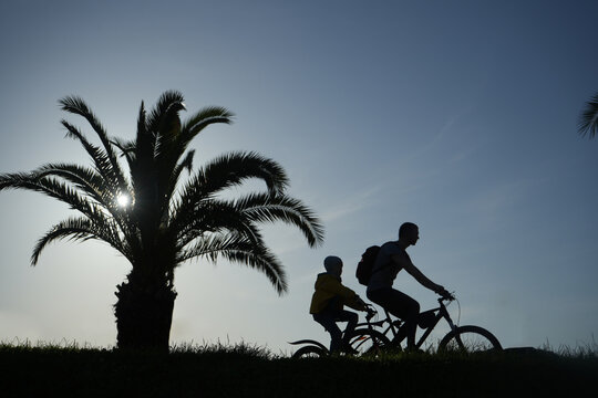 two biker - man and girl. couple silhouette of father and daughter in sunrise against blue sunset  on background. empty Space for inscription. sunlight through palm tree leaves. fresh green grass.