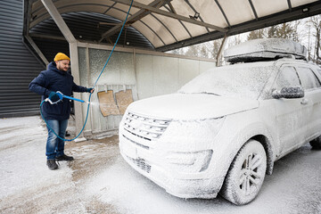 Man washing american SUV car with roof rack at a self service wash in cold weather.