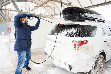 Man washing high pressure water american SUV car with roof rack at self service wash in cold...