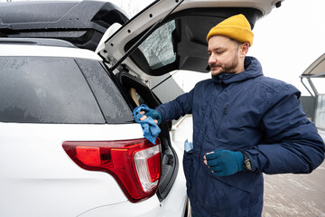 Man wipes trunk of american SUV car with a microfiber cloth after washing in cold weather.