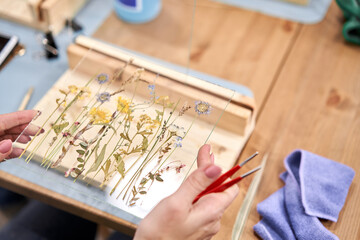A woman fixes glass plates.. Master class on creating frame with Herbarium in tiffany technique in stained glass. Herbarium of dried different plants and flowers placed under a glass - obrazy, fototapety, plakaty