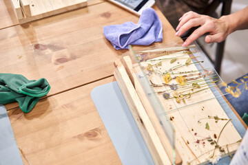 Master class on creating frame with Herbarium in tiffany technique in stained glass. A woman lays out a composition. Herbarium of dried different plants and flowers placed under a glass