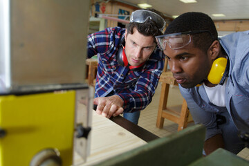 carpenter training male apprentice to use mechanized saw - obrazy, fototapety, plakaty