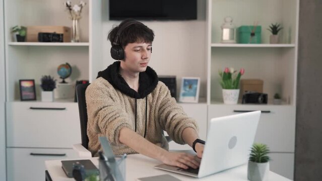 The young man, a sound engineer, sits behind his laptop. He listens to music that he enjoys and nods his head in rhythm.