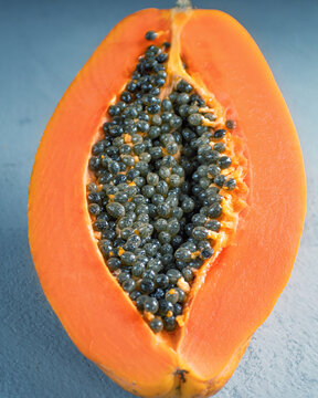 Half ripe and sweet papayo on a blue background.The papayo is orange in colour with black round seeds.
