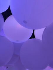 Grande salle remplie de grands ballons gonflables, fortement colorés de différentes couleurs, avec des personnages, plongés dans un univers sombre, flou, magique et envoûtant, musée numérique, teamlab