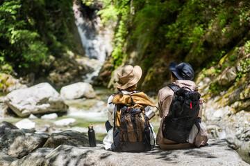 岩に座り滝を眺めながら休憩をしている登山者２人/
トレッキング