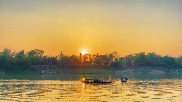Boats transporting villagers along river at sunrise with golden sky. Static wide