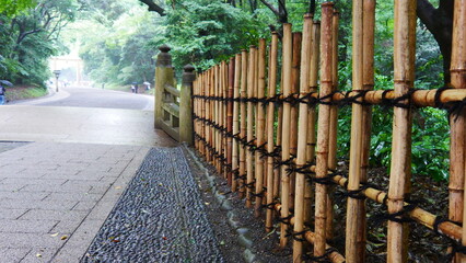 Barrière de bois construite manuellement, limitation naturelle et écologique entre le jardin et une zone forestière restreinte, sous un temps fort de pluie, sol humide et mouillé, avec habitation
