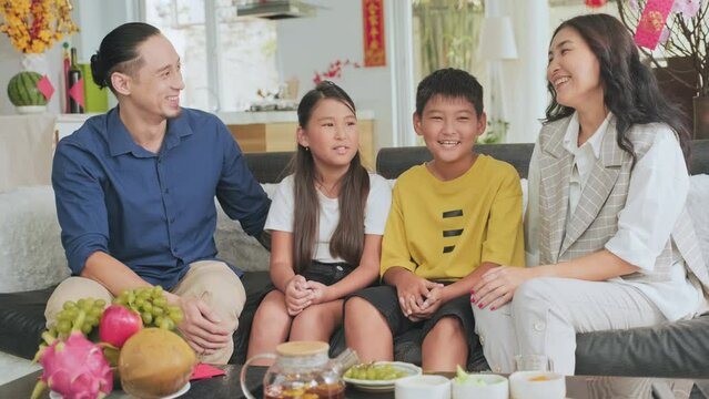 Asian parents, son and daughter sitting on sofa at home decorated for Tet holiday, smiling and chatting