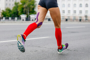 Fototapeta premium legs female runner athlete running marathon in city, compression socks on feet, kinesiotaping on knees for prevention