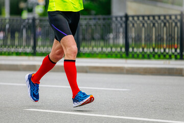 legs male runner athlete running marathon in city in red compression socks on feet, sports summer race