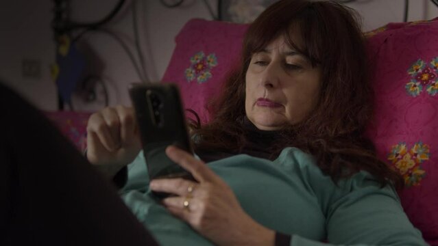 donna molto assonnata prova ad usare il suo smartphone mentre è a letto