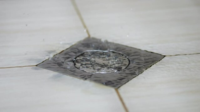 Running water clogs faulty metal drain grid in shower in tile bathroom. Water drops leave stains on clogged grey drain needing plumber to fix
