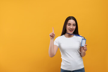 Smiling woman holding vip pass badge and pointing at something on orange background. Space for text