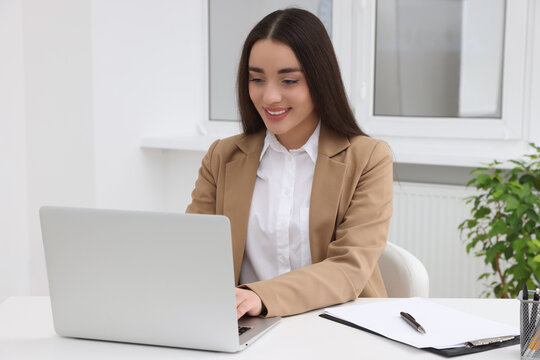 Young female intern working with laptop at table in office