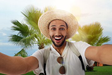 Smiling young man in straw hat taking selfie at resort