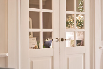Beautiful modern door knob. Christmas lights on the background. Open, wooden front door from the interior of an upscale home with windows.