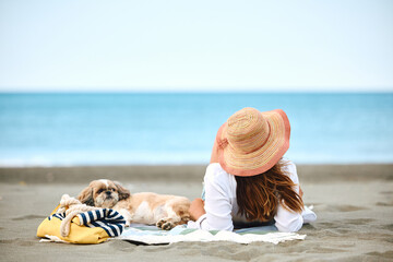 Rear view of woman with dog relaxing on sandy beach.