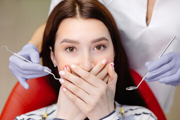 Closeup shot of a terrified female covering her mouth with both hands at the dentist appointment....