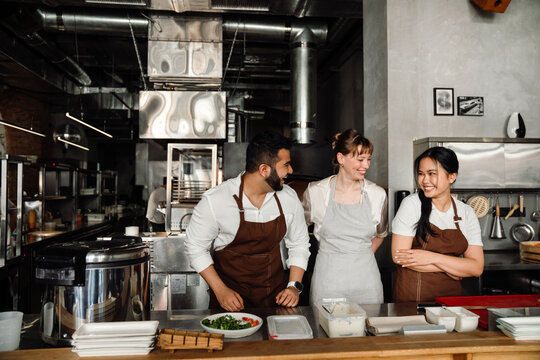 Handsome multiethnic chefs laughing while standing in kitchen