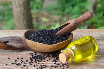Black cumin seeds and essential oil with bowl and wooden shovel or spoon. Nigella Sativa in glass...