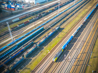 Cargo trains. Aerial view of colorful freight trains. Railway station. Wagons with goods on railroad. Heavy industry. Industrial scene with trains, city buildings and cloudy sky at sunset. Top view