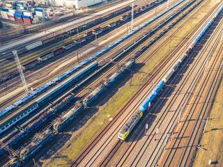 Cargo trains. Aerial view of colorful freight trains. Railway station. Wagons with goods on railroad. Heavy industry. Industrial scene with trains, city buildings and cloudy sky at sunset. Top view