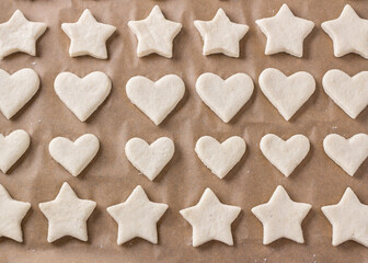 Raw cookies in the form of stars and hearts on a baking sheet with parchment, top view. Stage of cooking delicious homemade cakes - 604013415
