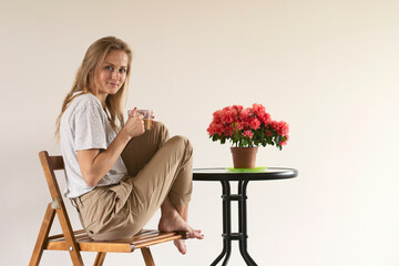 A girl drinks morning coffee at a table with an azalea flower