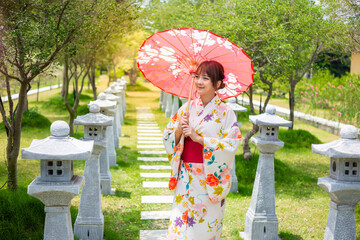 Young woman wearing a Japanese traditional kimono or yukata holding an umbrella in a garden with...