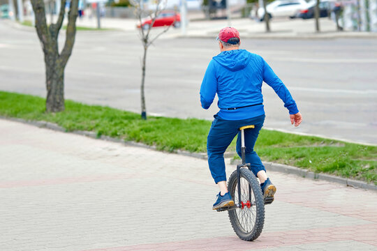 Man on unicycle moving along sidewalk. Elderly person ride on one wheel bike. Man riding monocycle at city street, active lifestyle.