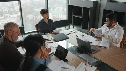 Overhead view of confident multinational team of colleagues gathered around table and discussing project in office - Powered by Adobe