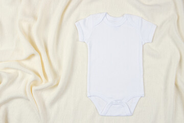 Top view to white cotton baby short sleeve bodysuit on beige blanket throw background. Infant onesie mockup. Blank gender neutral newborn bodysuit mock up template