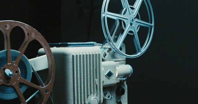 Old Movie Projector in Close up. Antique Movie Projector With 8mm Spinning Film Reels. Spinning Film Roll on a Vintage Film Projector. Light Beams From Film on an Old Projector 