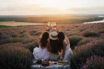 Group of happy young girlfriends clinking glasses with wine at the lavender field on beautiful...