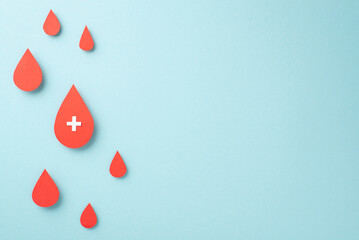 A pastel blue background with a top view of blood drops and a cross sign composition is the ideal...