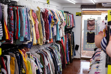 Lot of different bright summer clothes T-shirts, skirts, trousers, shirts hang on hangers in small private shop.