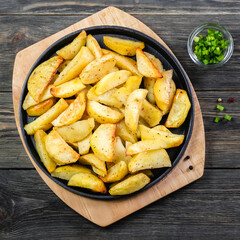 Crunchy air fryer potato wedges in cast iron skillet on wooden background. Top view, copy space, flat lay.